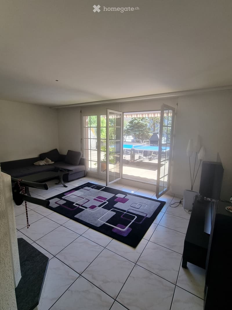 Living room with tiled floor, large sliding glass doors leading to a patio with a swimming pool, sofa, coffee table, television, and floor lamp.