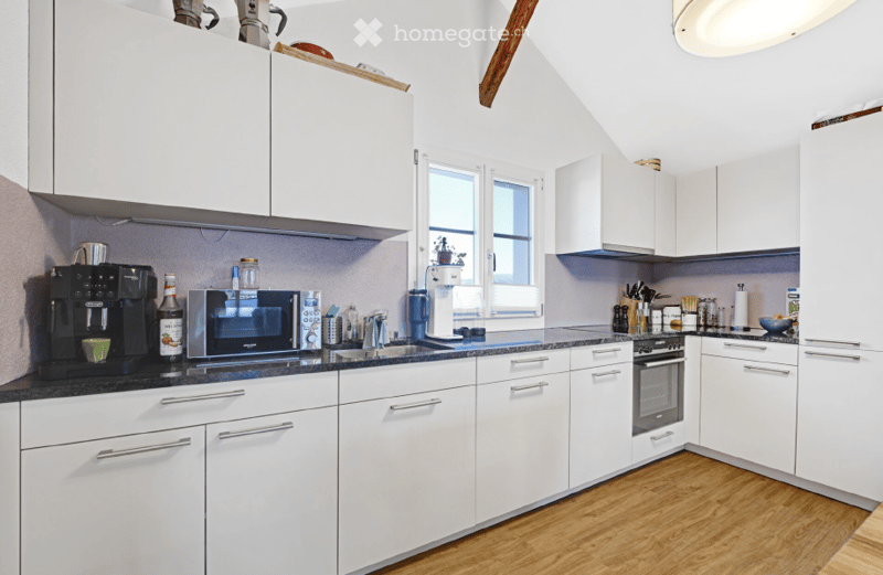 Modern kitchen with white cabinets, black countertop, coffee maker, microwave, oven, and various small appliances and items on the counter.