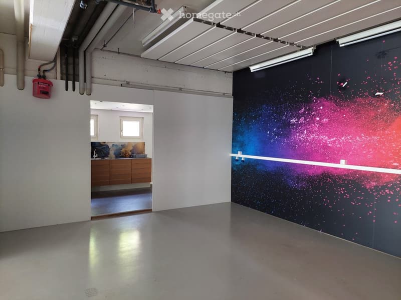 Open-plan space with a colorful mural on one wall, a kitchen area with cabinets and a sink, and a fire extinguisher mounted on the wall.
