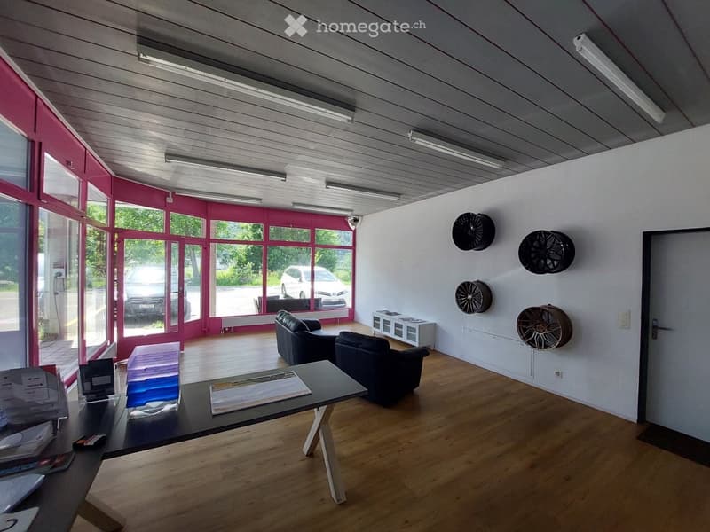 Modern, minimalist room with wooden flooring, large windows, and a sleek black sofa and table setup. Features a wall-mounted wheel display and a small cabinet.