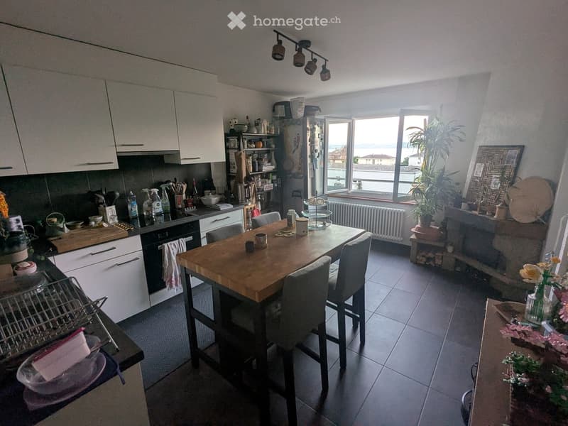 Modern kitchen with white cabinets, a wooden dining table with four chairs, and a view of the sea through large windows.
