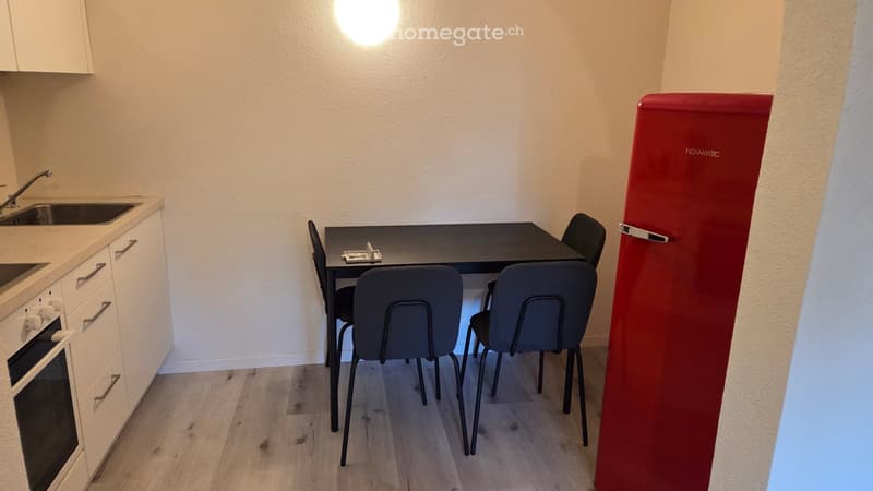 Compact kitchen area with a sink, faucet, oven, cabinets, a small dining table with four chairs, and a red refrigerator.