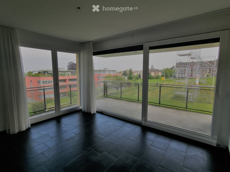 Empty room with dark tiled flooring, large windows with white curtains, and a view of a balcony and surrounding area.