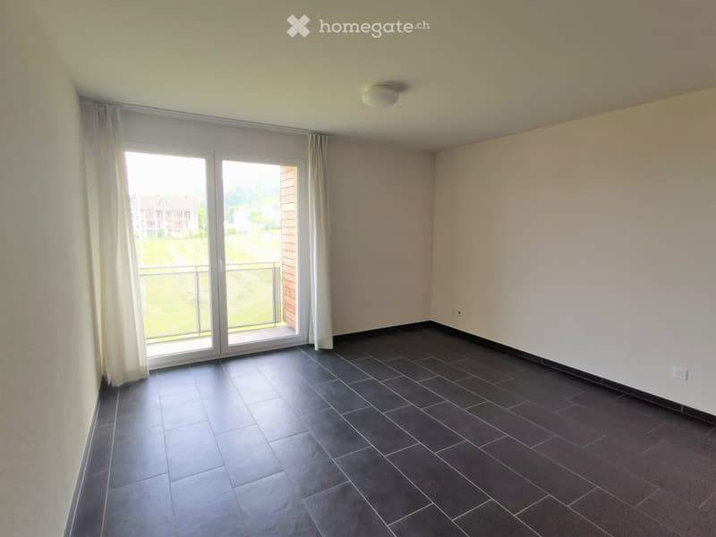 Empty room with dark tiled flooring, white walls, large sliding glass door with curtains, and a view of a green outdoor area.
