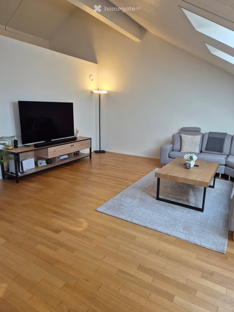 Modern living room with wooden flooring, grey sofa, coffee table, flat-screen TV on a wooden stand, and a floor lamp.