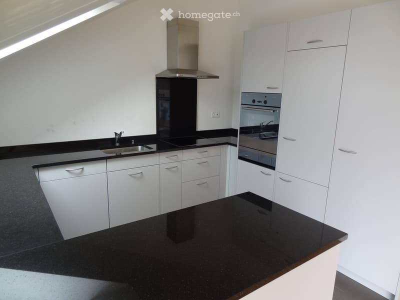 Modern kitchen with white cabinets, black countertops, stainless steel sink, oven, and range hood.