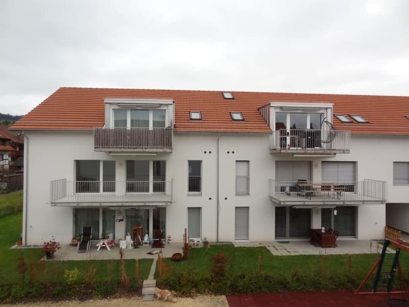 Two-story white house with red-tiled roof, multiple balconies, and a well-maintained garden area.