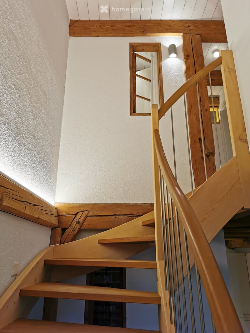 Wooden staircase with a handrail and a mirror on the wall, illuminated by recessed lighting.