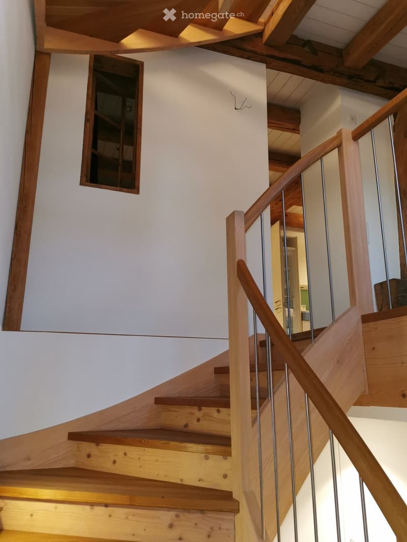 Wooden staircase with metal railing, light-colored walls, and exposed wooden beams on the ceiling.