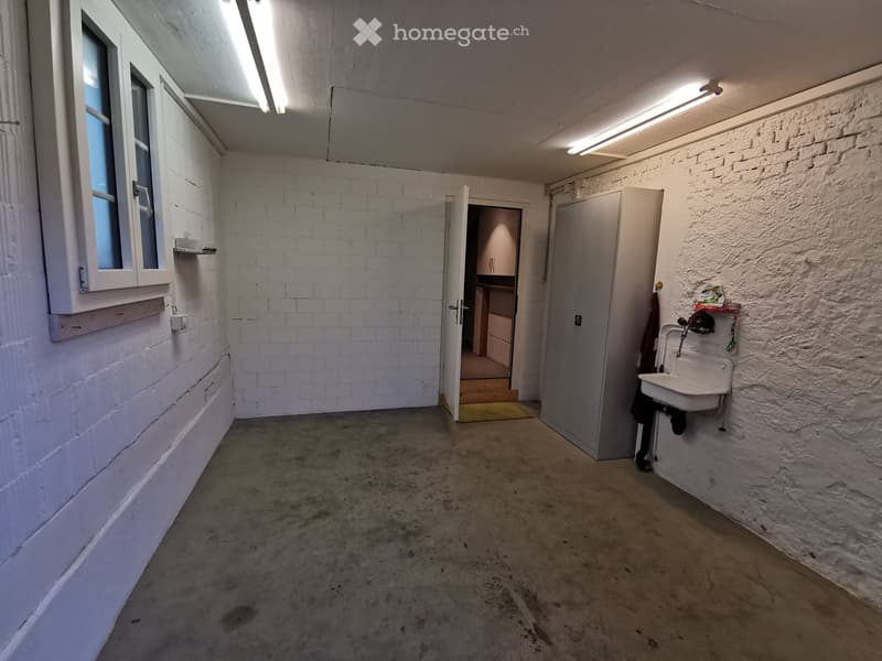 Empty room with white brick walls, concrete floor, and a small sink in the corner. There is a window with white frames and a door leading to another room.