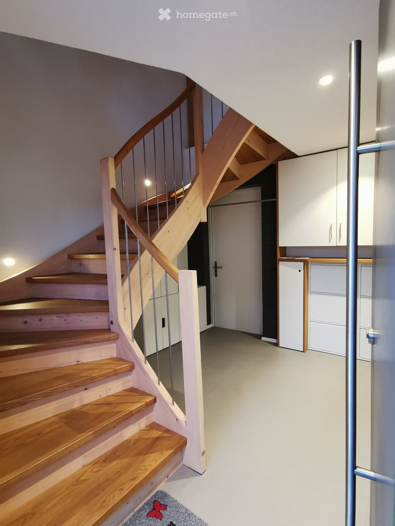 Modern hallway with wooden staircase, white cabinets, and a small rug on the floor.
