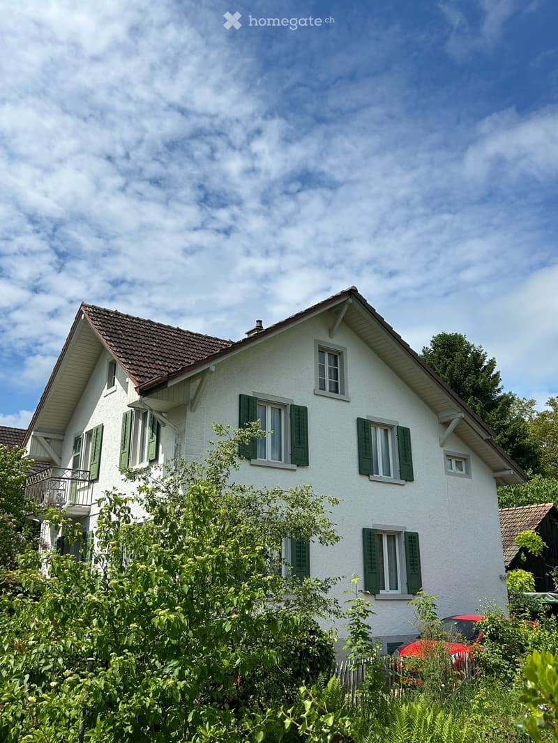 Two-story white house with green shutters, red-tiled roof, and balcony on the left side.