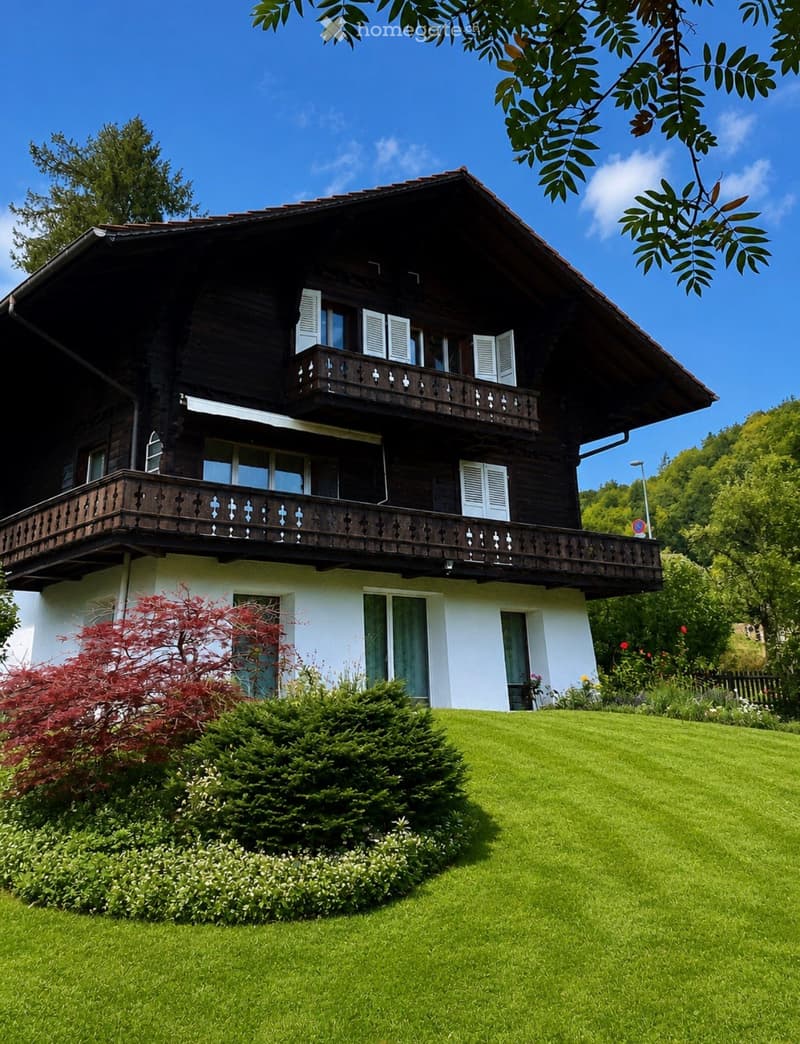Two-story wooden house with white shutters, balconies, and a well-maintained garden with green lawn and shrubs.