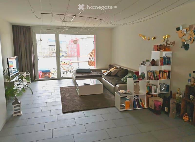 Modern living room with a grey sectional sofa, white coffee table, bookshelf, and large sliding glass doors leading to a balcony.
