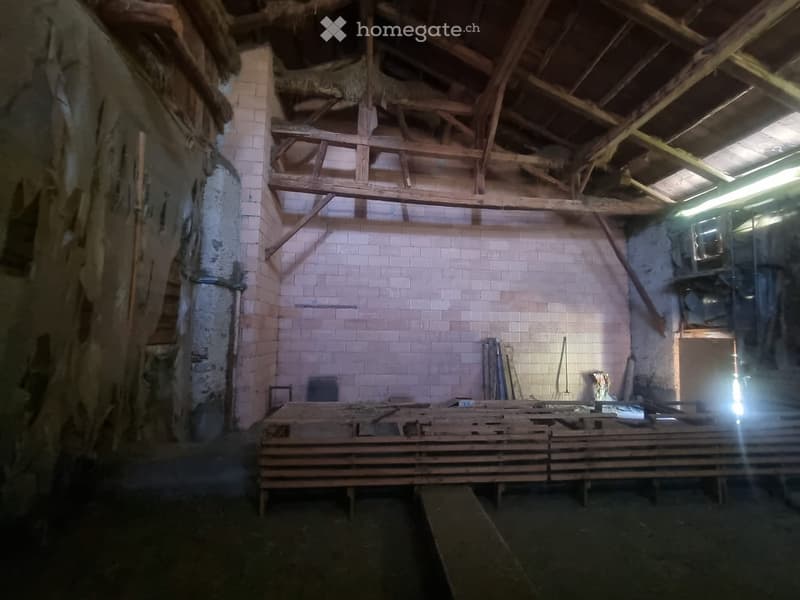 Empty room with exposed wooden beams and brick walls, featuring a large wooden workbench and scattered tools.