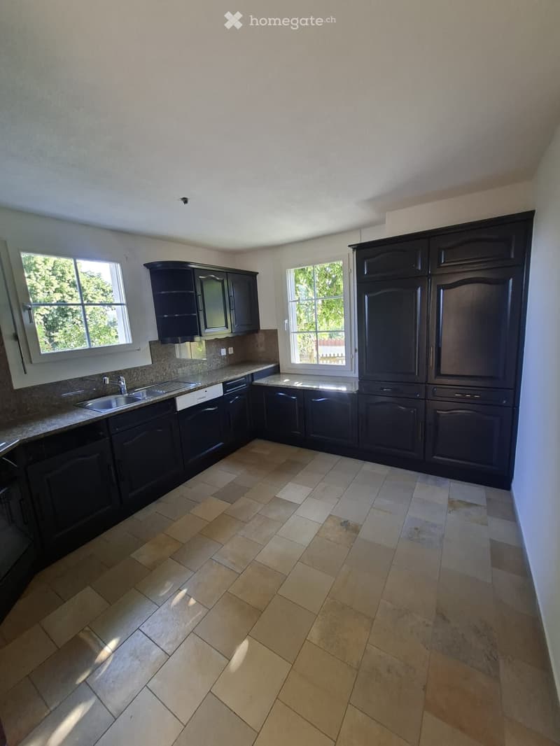 Empty kitchen with dark wooden cabinets, a tiled floor, and two windows letting in natural light.