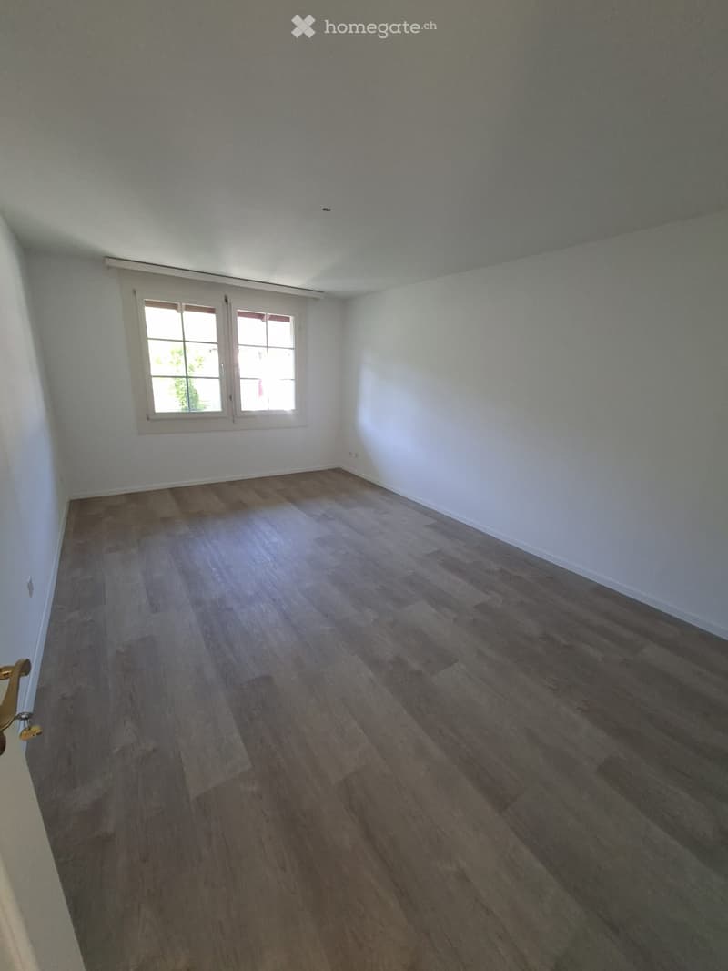 Empty room with wooden flooring, white walls, and a window with blinds.