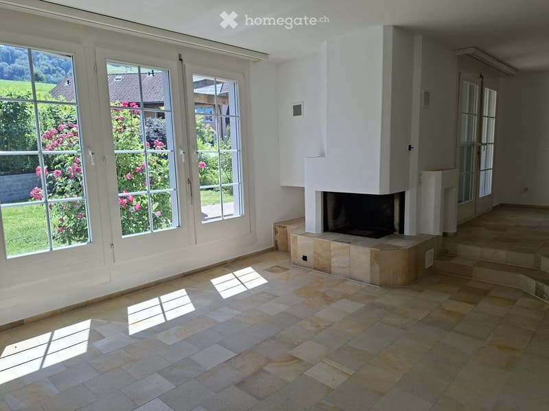 Bright, unfurnished room with large windows, tiled floor, and a built-in fireplace.