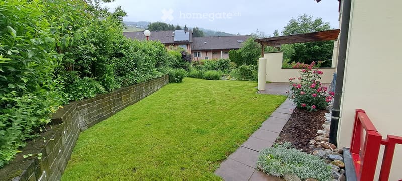 Well-maintained garden with a neatly trimmed lawn, a brick border, and a variety of plants and flowers. A covered patio area is visible in the background.