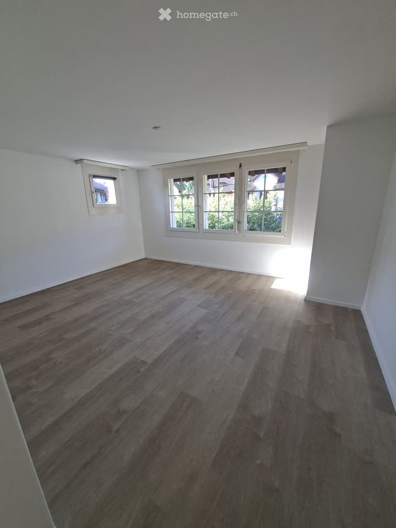 Empty room with wooden flooring and white walls, featuring multiple windows allowing natural light to enter.