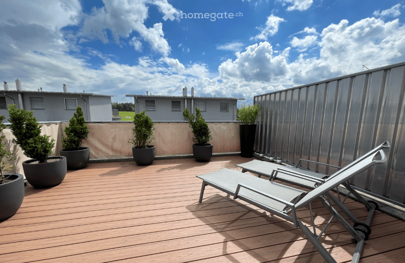 Wooden deck with sun loungers and potted plants, modern metal railing, clear sky view.