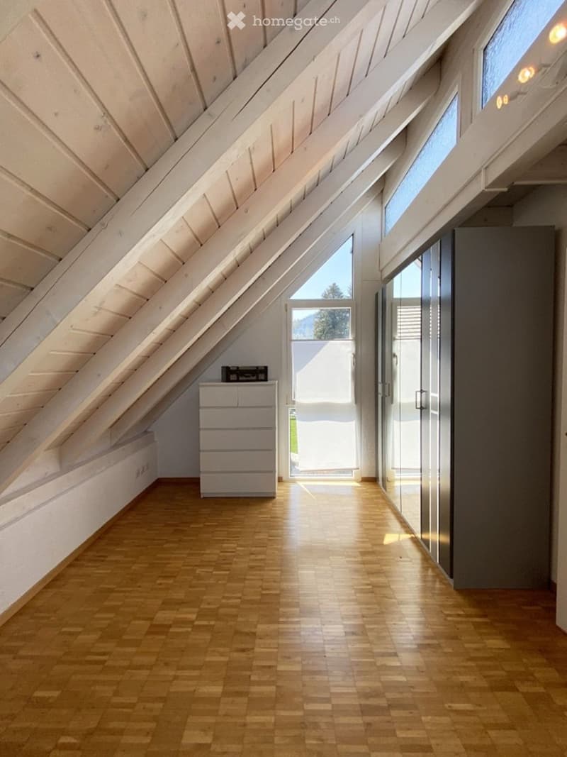 Furnished Room. Bright attic room with wooden flooring, slanted white wooden ceiling, large windows, and a small drawer unit near the entrance.