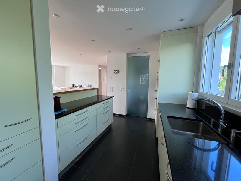 Modern kitchen with white cabinets, black countertops, and a double sink. The space features sleek, contemporary design with a large window providing natural light.