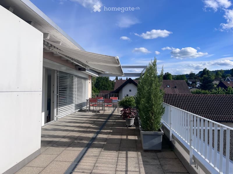 Balcony with a retractable awning, seating area with chairs and a table, and potted plants.