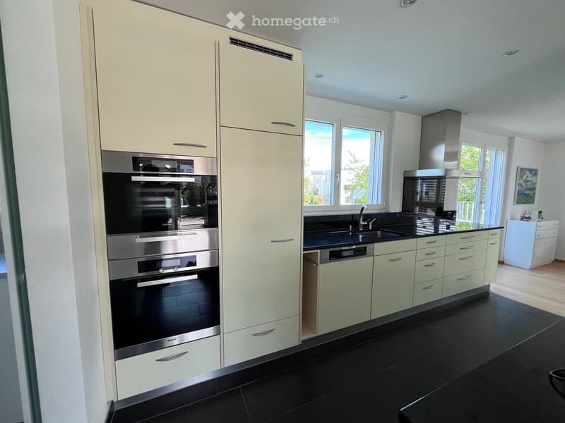 Modern kitchen with light-colored cabinets, stainless steel appliances, black countertops, and a large window letting in natural light.