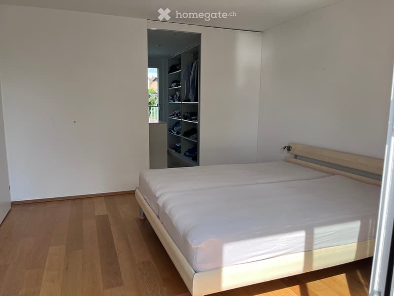 Bright bedroom with a double bed, light wooden floor, and built-in wardrobe with shelves.