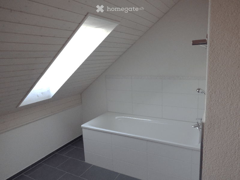 Bathroom with a white bathtub, tiled walls, and a skylight window providing natural light.