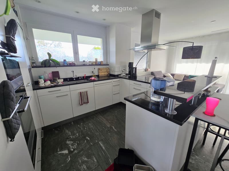 Modern kitchen with white cabinets, black countertops, and a central island. Features include a sink, coffee maker, and various kitchen items on the counters.