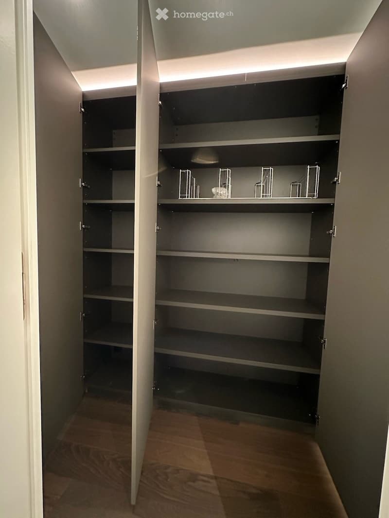 Empty closet with multiple shelves and built-in storage units, wooden flooring, and soft lighting from integrated LED strips.