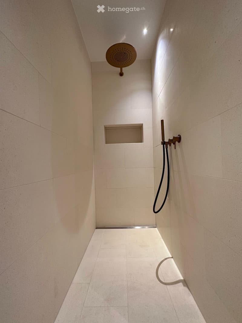 Modern shower area with light-colored tiles, a round showerhead, and a handheld shower hose.