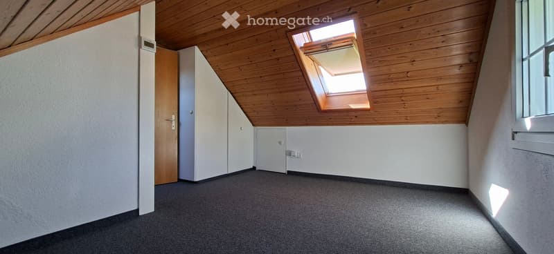 Empty room with wooden slanted ceiling, grey carpet, white walls, and a skylight window.