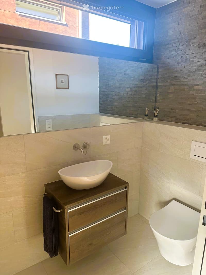 Modern bathroom with a sleek sink, wooden cabinet, and a bathtub. Features a large mirror, a towel, and a stylish faucet.