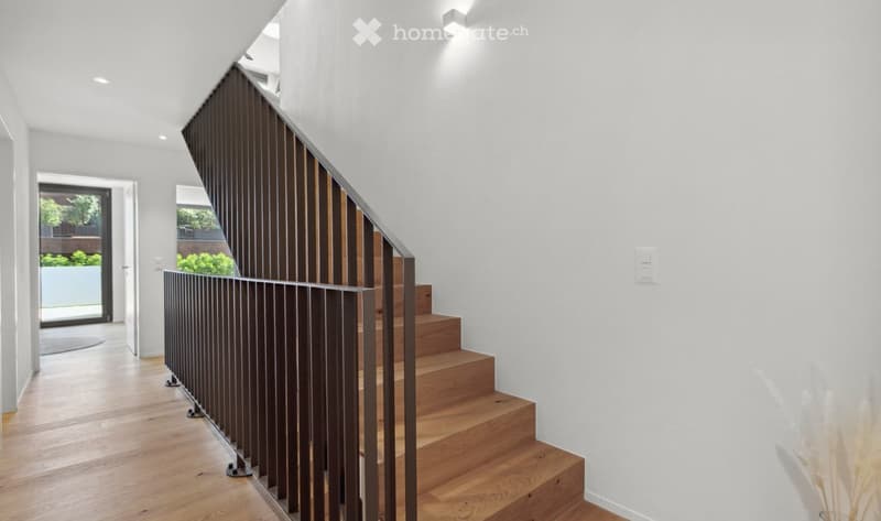 Modern hallway with wooden staircase, sleek metal railing, white walls, recessed lighting, and a view of a garden through a glass door.