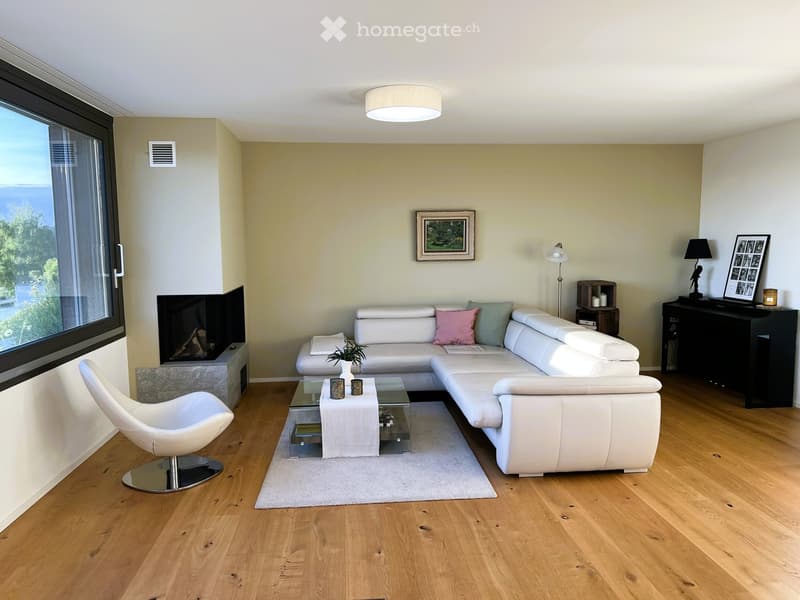 Modern living room with white leather sofa, glass coffee table, white armchair, fireplace, large windows with ocean view, and decorative items.