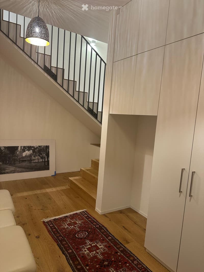 Modern hallway with wooden flooring, a staircase leading upwards, a pendant light, a sofa, a picture frame, and built-in cabinets.