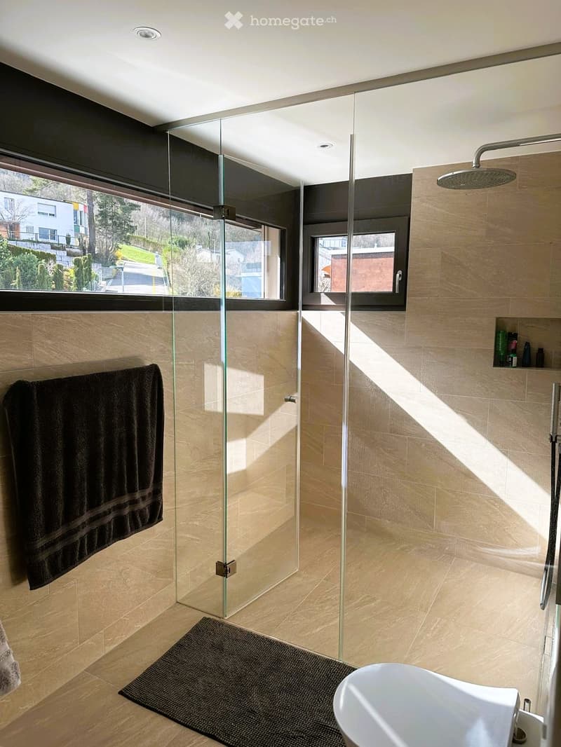 Modern bathroom with a glass-enclosed shower, a bathtub, a towel on the wall, and a small shelf with toiletries.