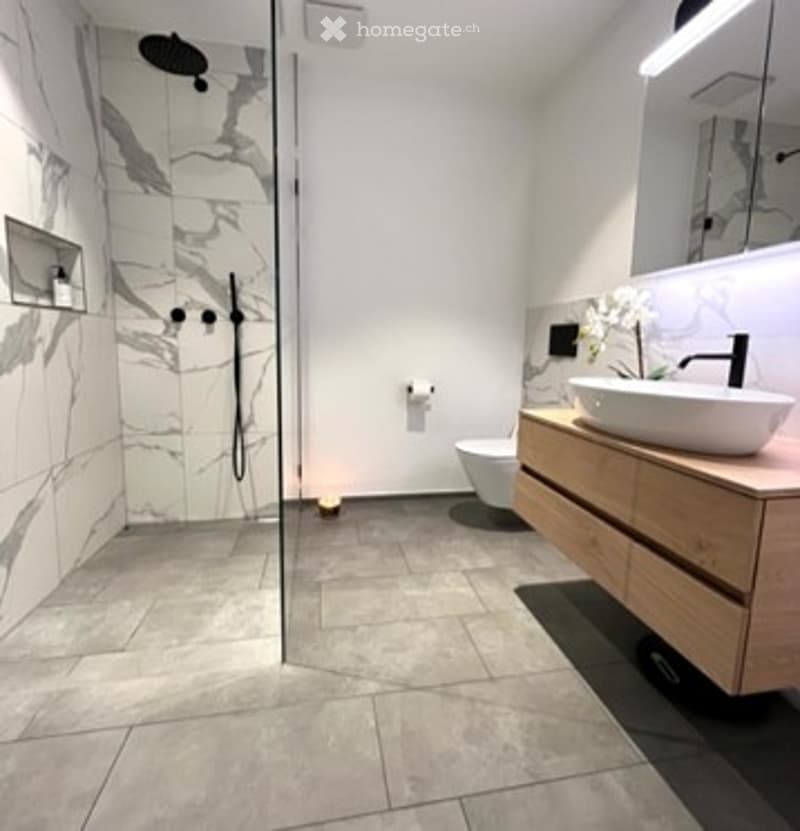 Modern bathroom with marble tiles, glass shower enclosure, floating vanity, and sleek fixtures.