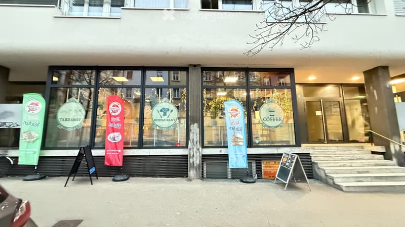 Facade of a multi-story building with large windows, signage for a restaurant, takeaway, and coffee shop, and festive decorations visible inside.