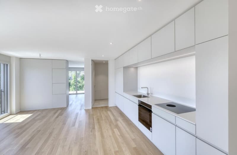 Modern, minimalist kitchen with white cabinets, light wooden flooring, and built-in appliances including a sink, oven, and stove.