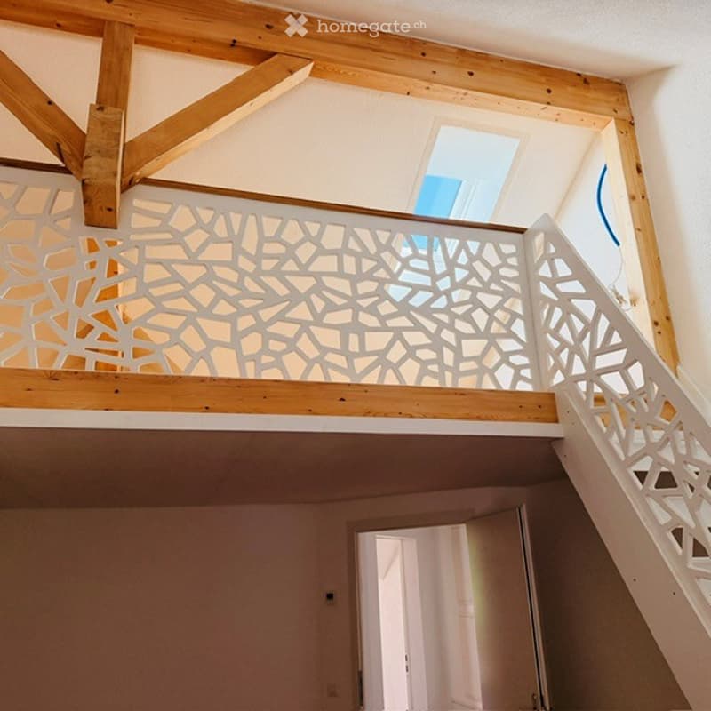 Modern interior view of a hallway with exposed wooden beams and a decorative white lattice railing leading to an open area with natural light.