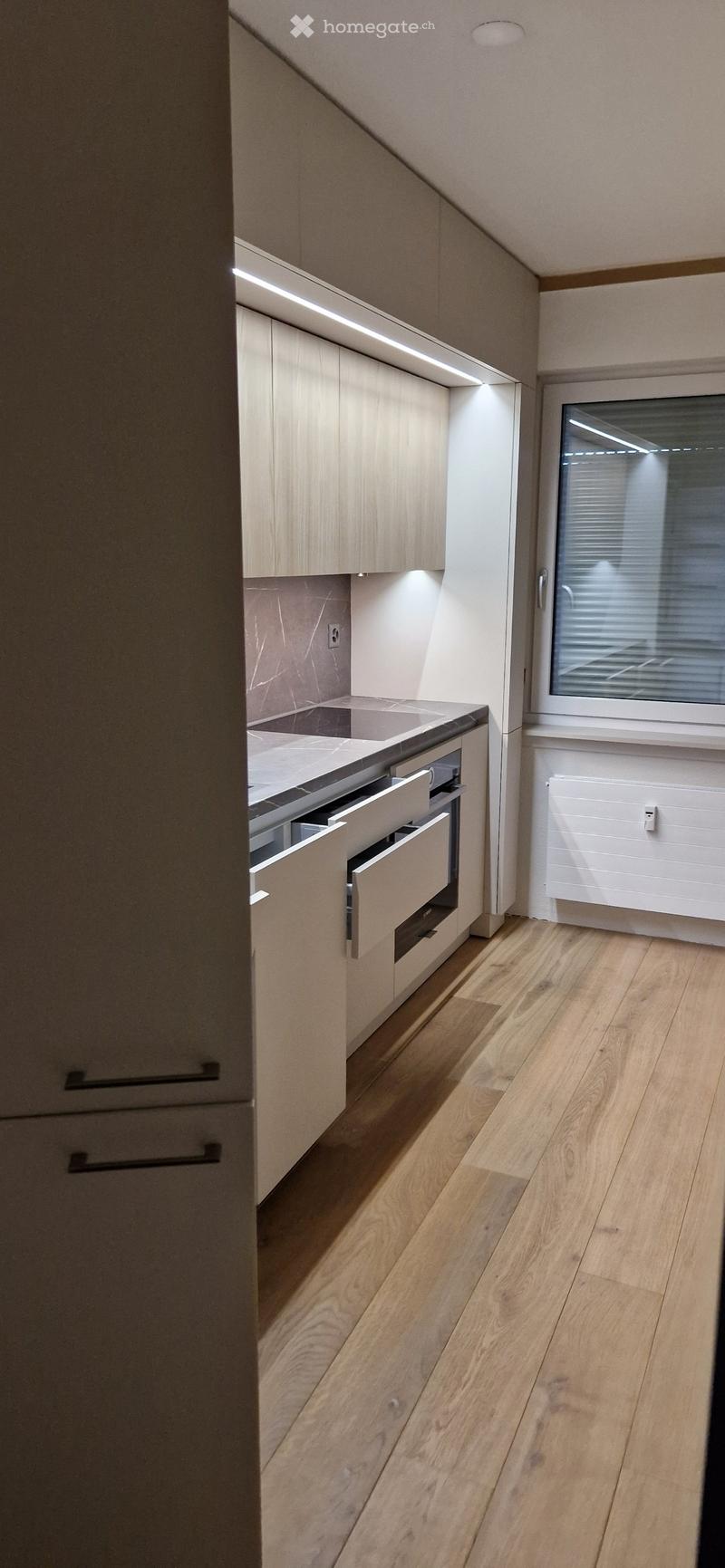 Modern kitchen with light wood cabinets, stainless steel sink, and built-in drawer, featuring a sleek design and warm lighting.