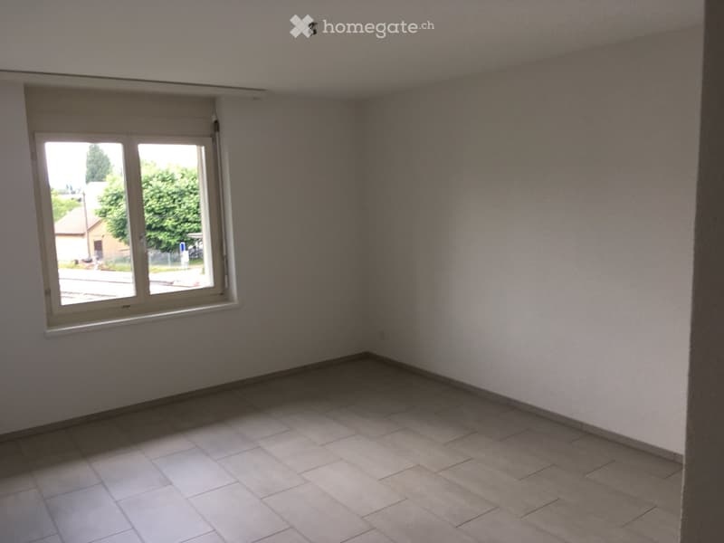 Empty room with tiled floor and large window letting in natural light. Bare walls and no furniture.