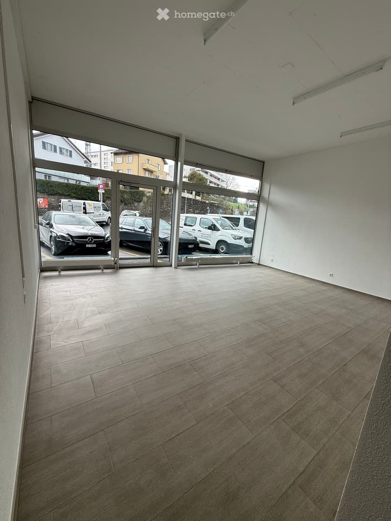 Empty room with large glass doors leading to a parking area, tiled floor, and white walls.