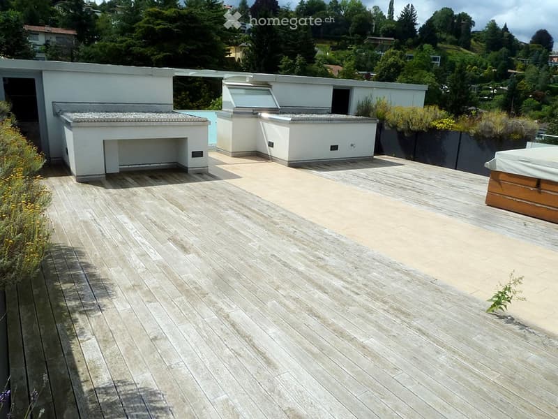Roof terrace with wooden decking, built-in barbecue, small seating area, and hot tub, overlooking a green, hilly landscape.