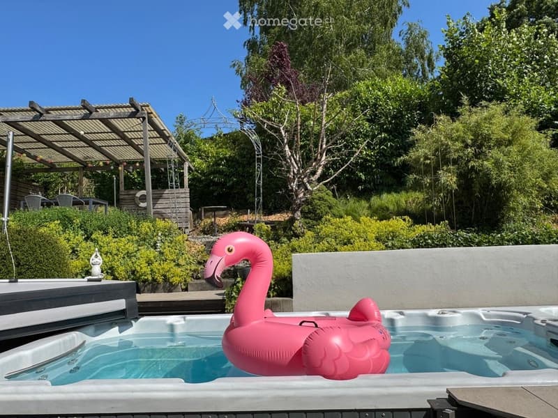 Garden area with a hot tub, pink inflatable flamingo float, covered patio, and lush greenery.