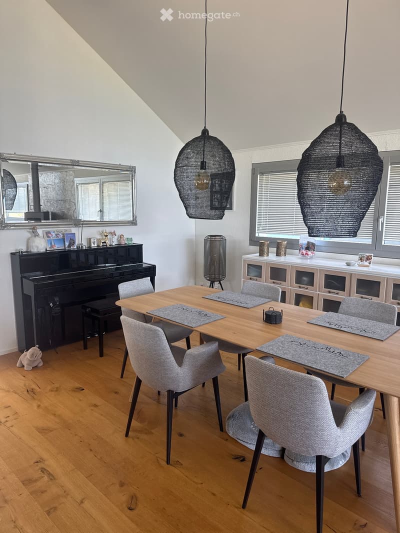 Dining area with wooden table, six chairs, piano, mirror, and decorative items on shelves.